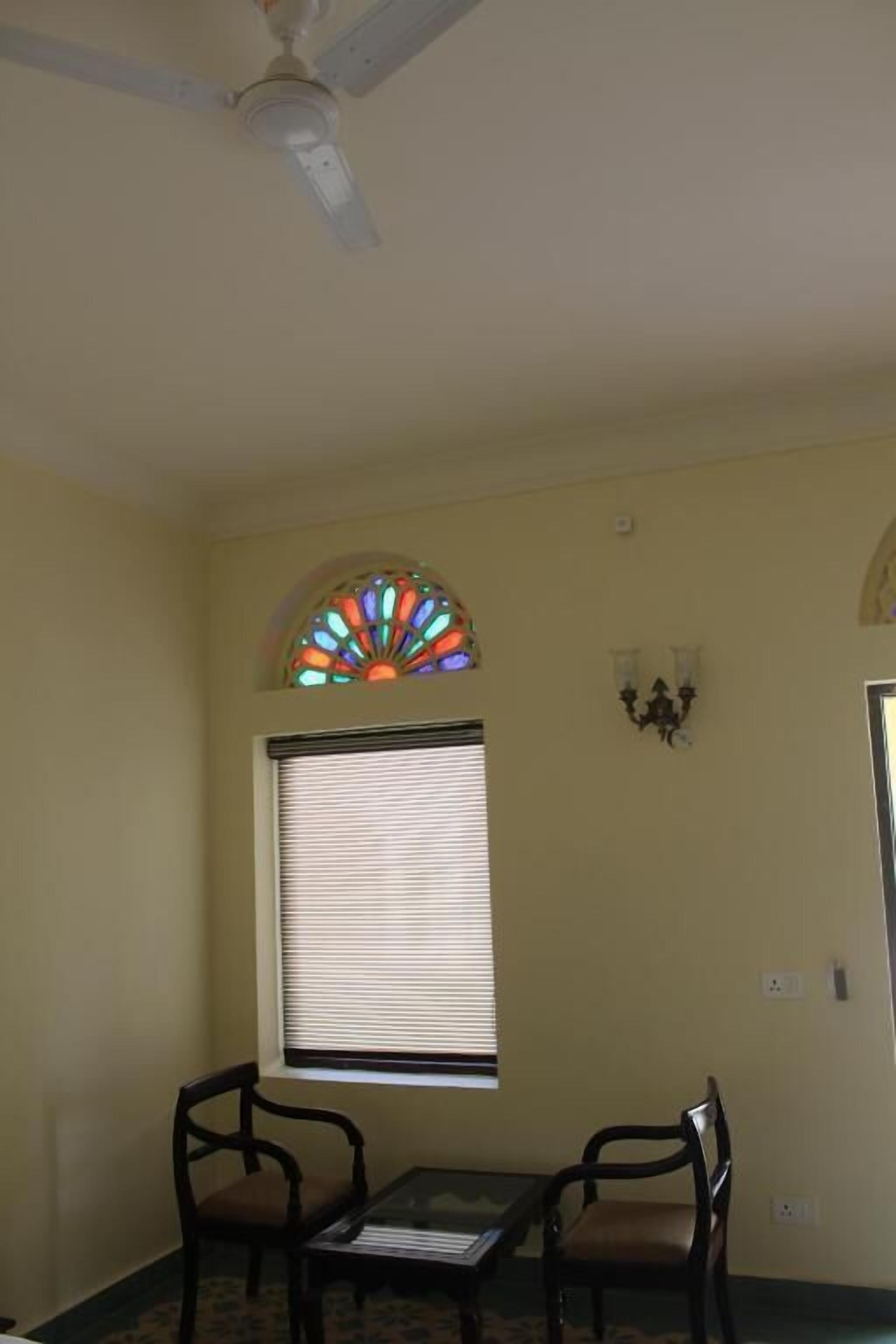 A room with a ceiling fan, a stained glass window, two chairs, a table, and a wall-mounted light fixture.
