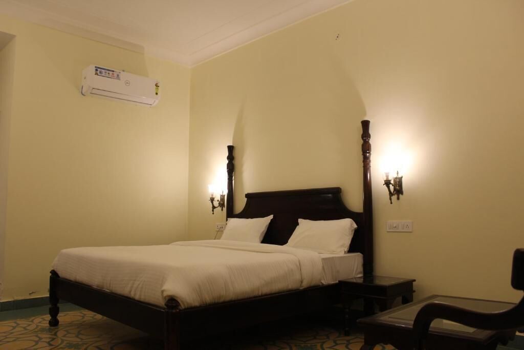 A hotel room with a four-poster bed, bedside lamps, a small table, and an air conditioning unit on the wall.