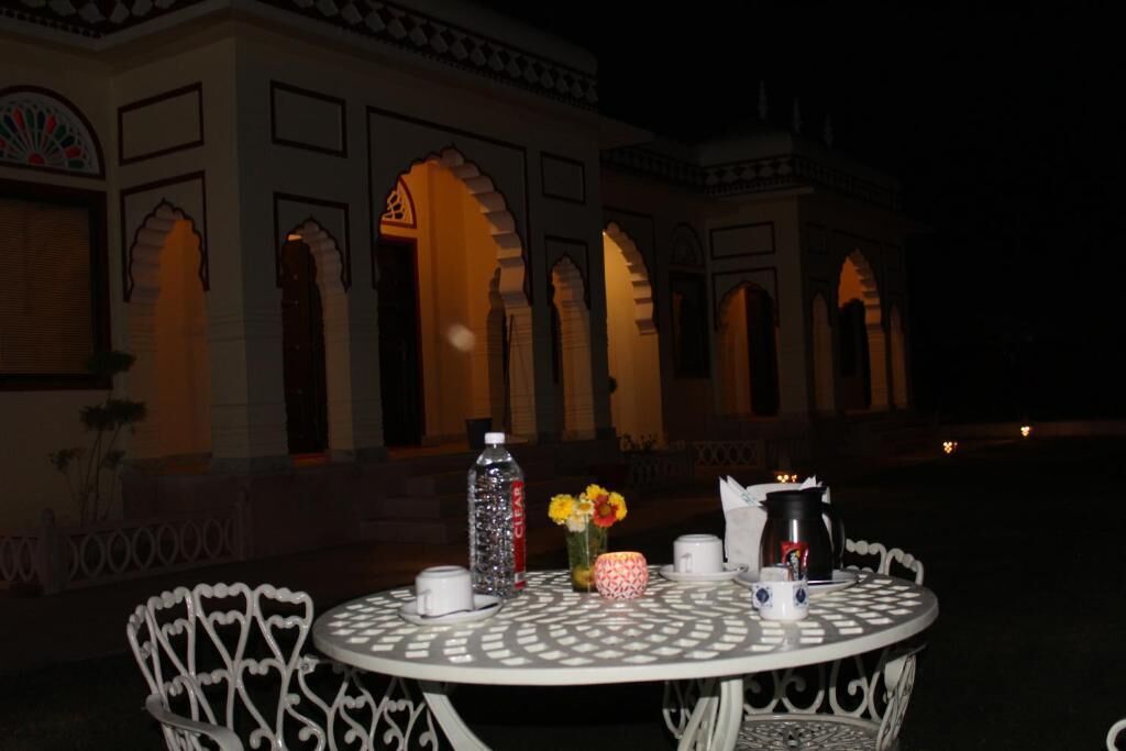 An outdoor dining area with a round table and white chairs, set against a building with arches and a night sky.