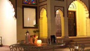 Un espacio exterior bien iluminado con una mesa y sillas, un ventanal decorativo y una puerta con un arco.