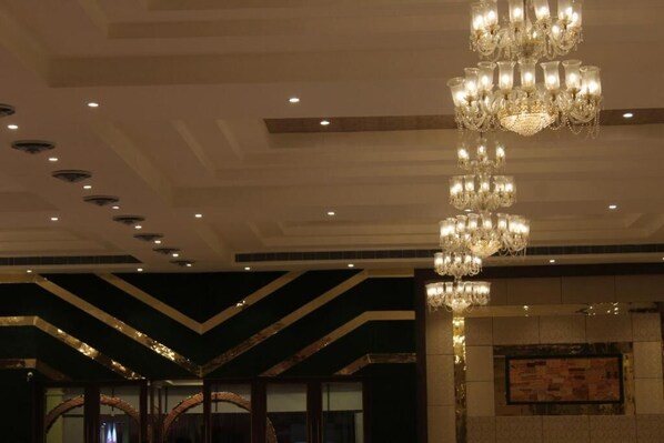 Un candelabro con varios niveles y luces, un techo con iluminación empotrada y una pared con diseño y un tablón de anuncios.