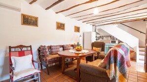 A cozy living room with a wooden dining table, a sofa with patterned cushions, and a chair. There is a staircase leading to an upper level. - La Casa de Aulabar Belmez de la Moraleda by Ruralidays (Jaén)