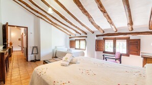 A bedroom with a large bed, a smaller bed, wooden beams, a window with shutters, and a chair. - La Casa de Aulabar Belmez de la Moraleda by Ruralidays (Jaén)
