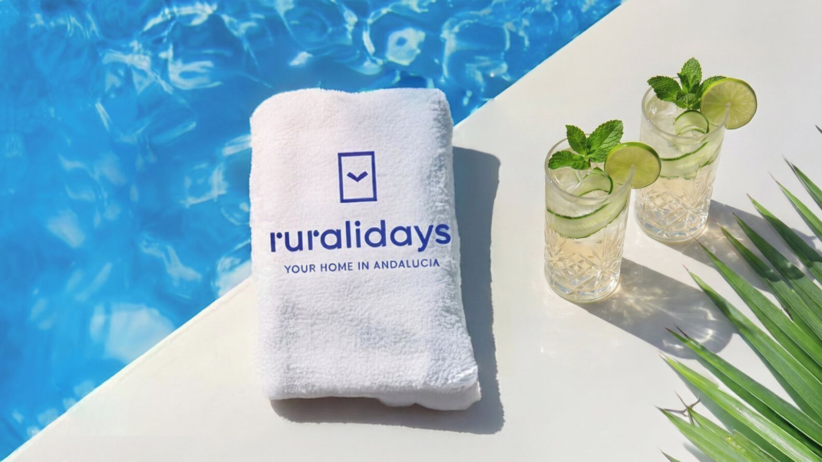 A poolside setting with a towel, two glasses of a beverage with lime and mint, and a logo on the towel.