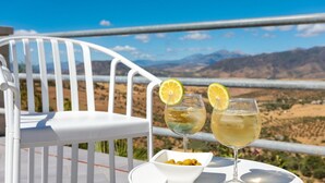 A white chair and two glasses of a light-colored drink with lemon slices, a small bowl of olives, and a scenic view of mountains and a valley. - Villa Rural el Mirador Álora by Ruralidays (Málaga)