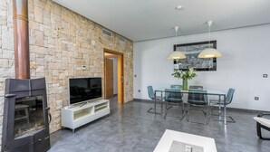 A modern living room with a stone wall, a fireplace, a flat-screen TV, a glass dining table with chairs, and pendant lights. - Villa Rural el Mirador Álora by Ruralidays (Málaga)