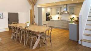 A spacious kitchen with wooden beams, a dining area with a wooden table and chairs, and a staircase. - Olivers Barn - UK42081 (Shefford Woodlands Near Hungerford)