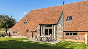 A two-story house with a sloped roof, a patio with outdoor furniture, and a large sliding glass door. - Olivers Barn - UK42081 (Shefford Woodlands Near Hungerford)