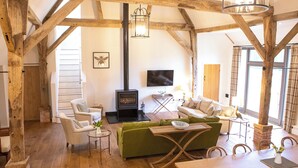 A rustic interior with exposed wooden beams, a fireplace, a sofa, a dining table, and a television. - Olivers Barn - UK42081 (Shefford Woodlands Near Hungerford)