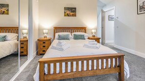 Un dormitorio con una cama grande, dos mesitas de noche, un espejo y una puerta que da a otra habitación.