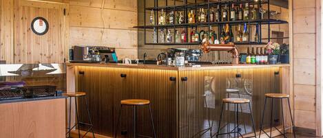 A bar area with wooden paneling, a coffee machine, and multiple stools.