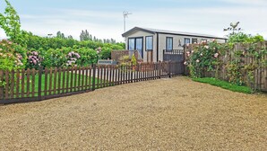 Une maison moderne avec une allée en gravier, entourée d’une clôture en bois et d’une végétation luxuriante.