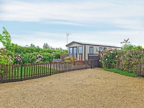 Ein modernes Haus mit Kiesauffahrt, umgeben von einem Holzzaun und üppiger Bepflanzung.