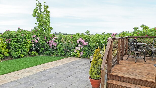 Une terrasse carrelée, une plateforme en bois et un jardin agrémenté de diverses plantes et fleurs.