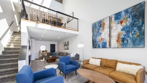 A spacious living area with a staircase, a blue armchair, a brown sofa, and abstract art on the wall. - Spacious, Updated Mountain Home with Views, Private Hot Tub and Sauna. (Fraser)