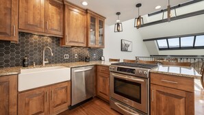 A modern kitchen with wooden cabinets, a stainless steel dishwasher, an oven, and a large island with a sink. - Spacious, Updated Mountain Home with Views, Private Hot Tub and Sauna. (Fraser)