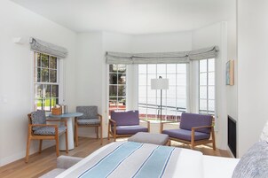 Una habitación luminosa con una cama, dos sillas, una mesita y un ventanal grande.