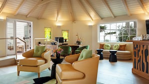 A spacious living area with high ceilings and wooden beams, featuring leather armchairs, a sofa, and a coffee table.