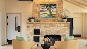 A spacious living room with a stone fireplace, two armchairs, and a large painting above the fireplace.