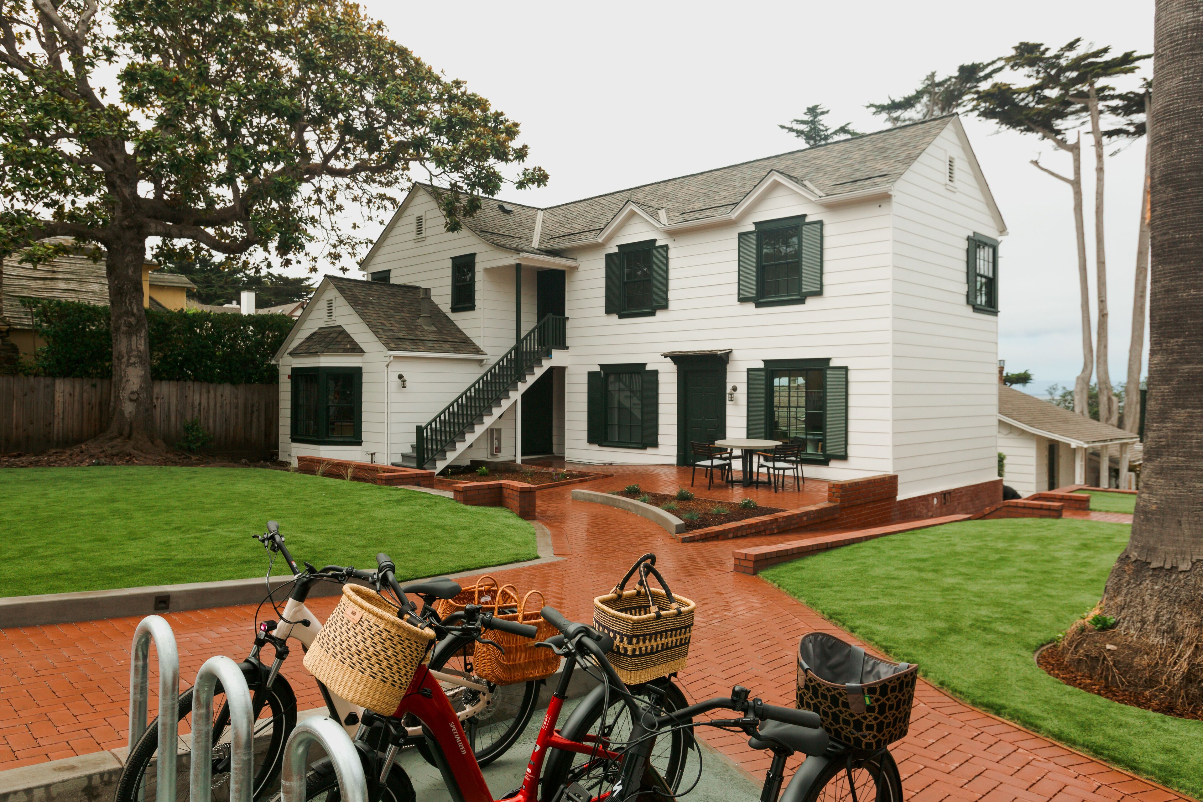 A two-story white house with a brick pathway leading to the front door, a staircase, and a small outdoor seating area.