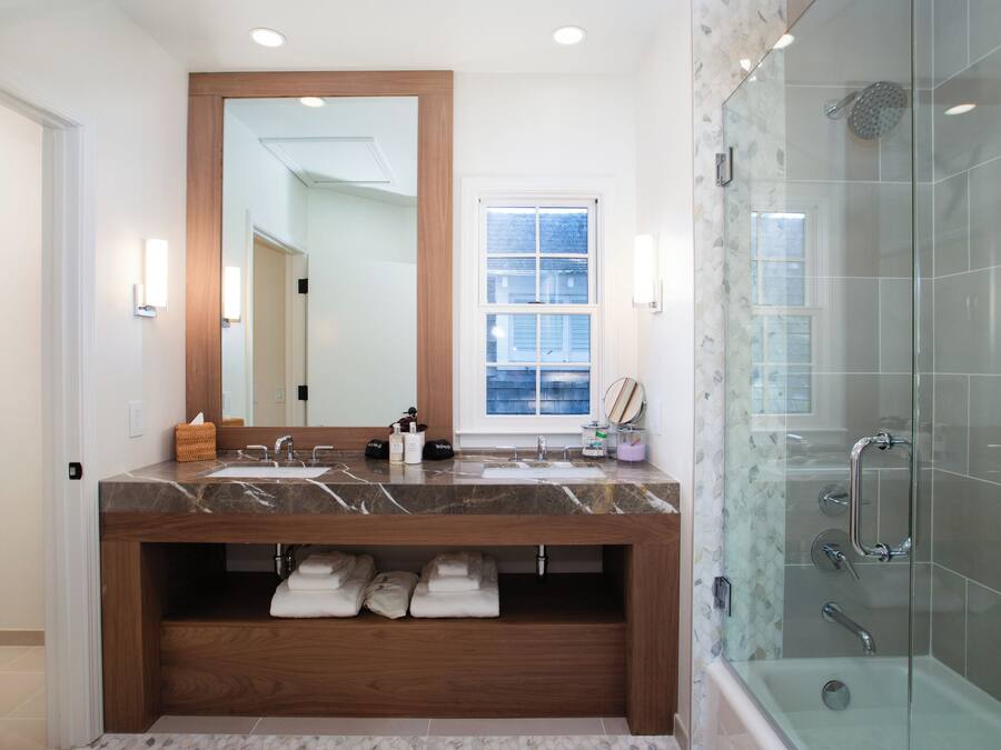 A modern bathroom with a marble sink, wooden vanity, glass shower enclosure, and a large mirror.