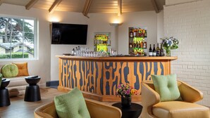 A modern living room with a high ceiling, a bar area with a zebra-patterned countertop, and a large window offering a view of the outdoors.