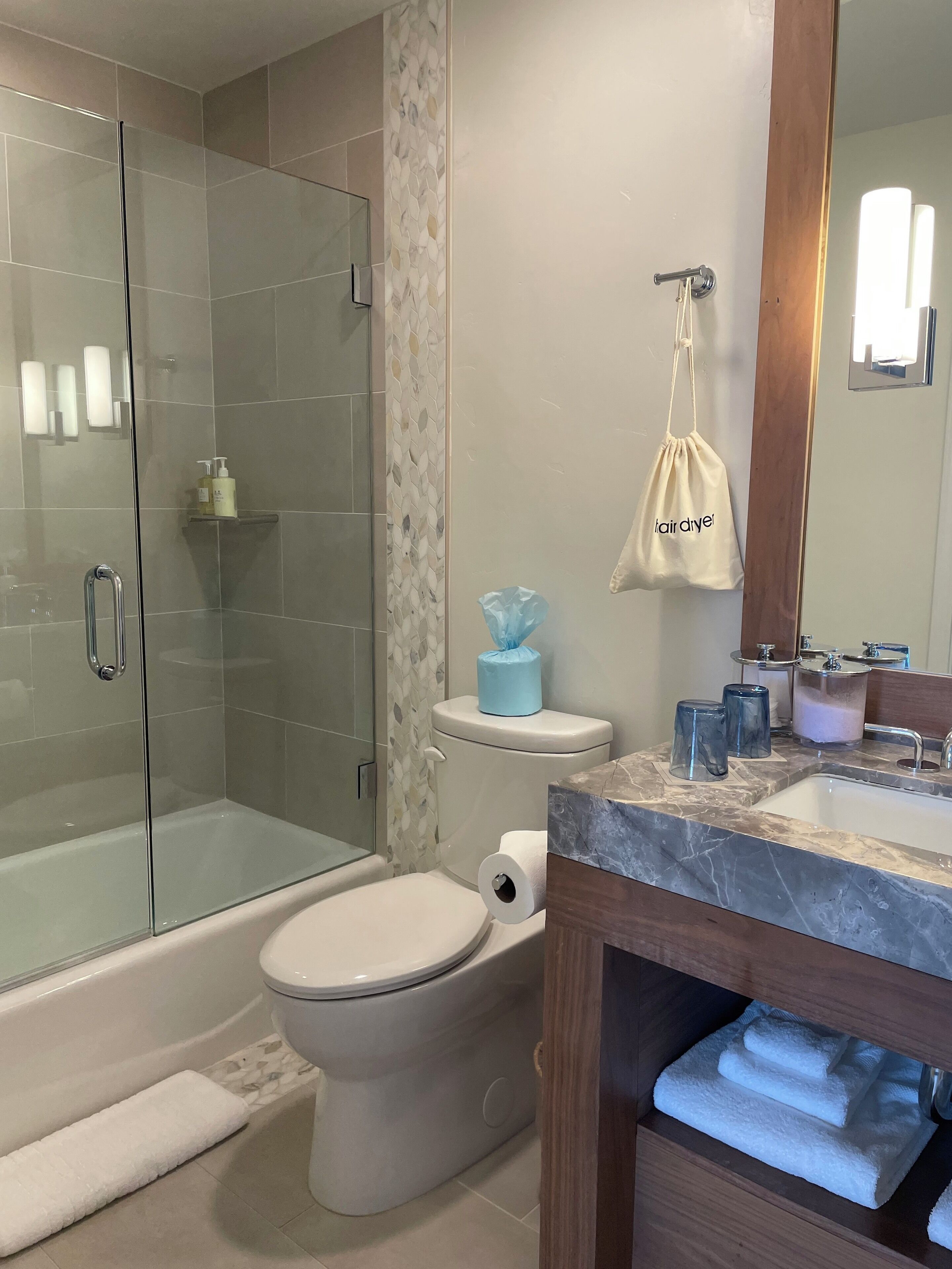 Un baño moderno con cabina de ducha de vidrio, inodoro, lavabo con encimera de mármol y tocador de madera.