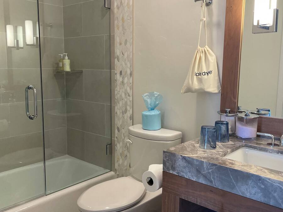 Un baño moderno con cabina de ducha de vidrio, inodoro, lavabo con encimera de mármol y tocador de madera.