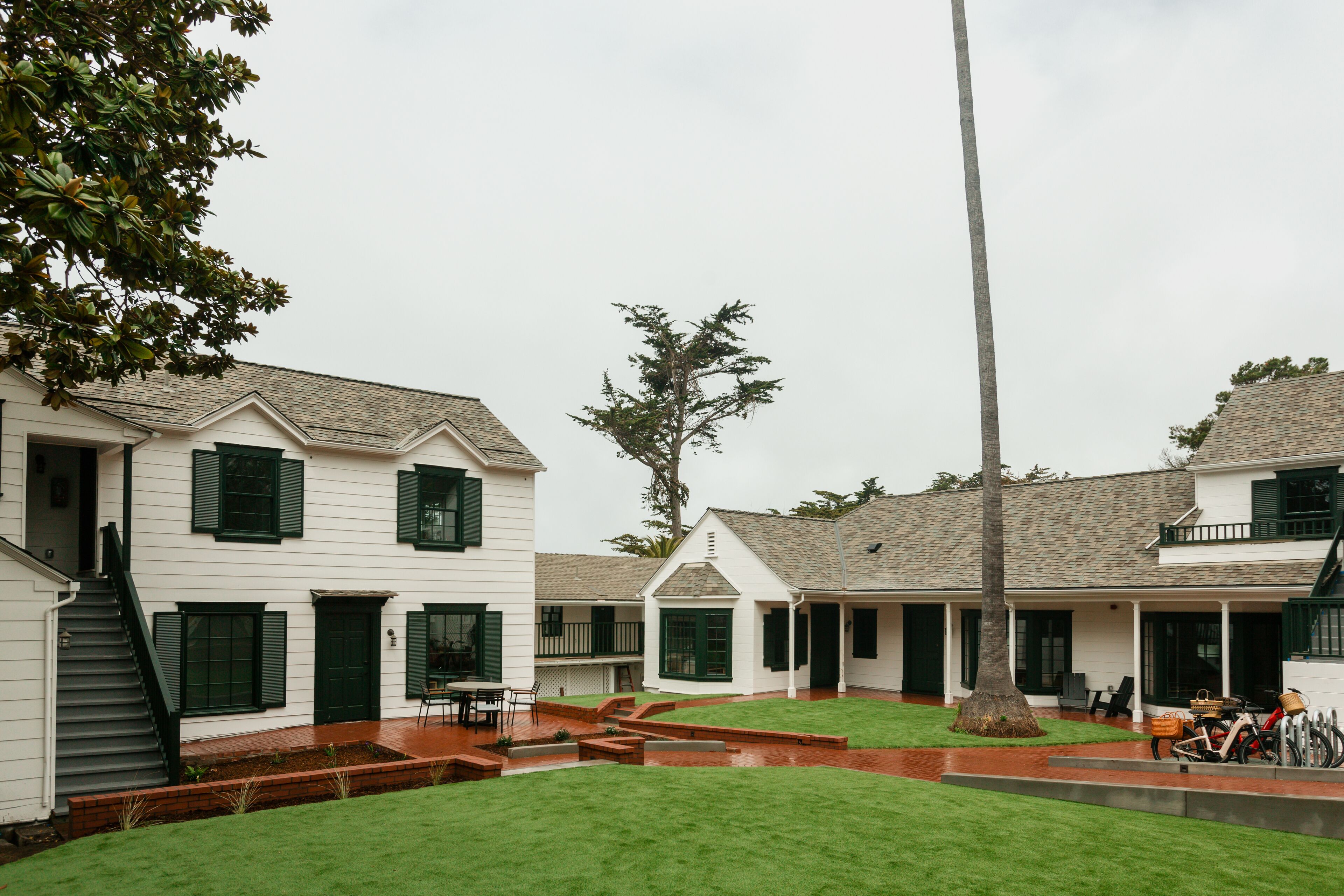 A white building with green shutters, a covered patio, and a well-maintained lawn.
