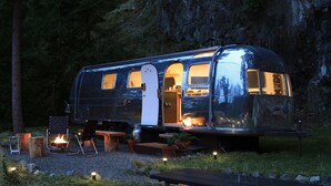 A vintage camper with a kitchen area, a dining table, and a fire pit. - Wildernest Mountainside Airstream Getaway (Bowen Island)
