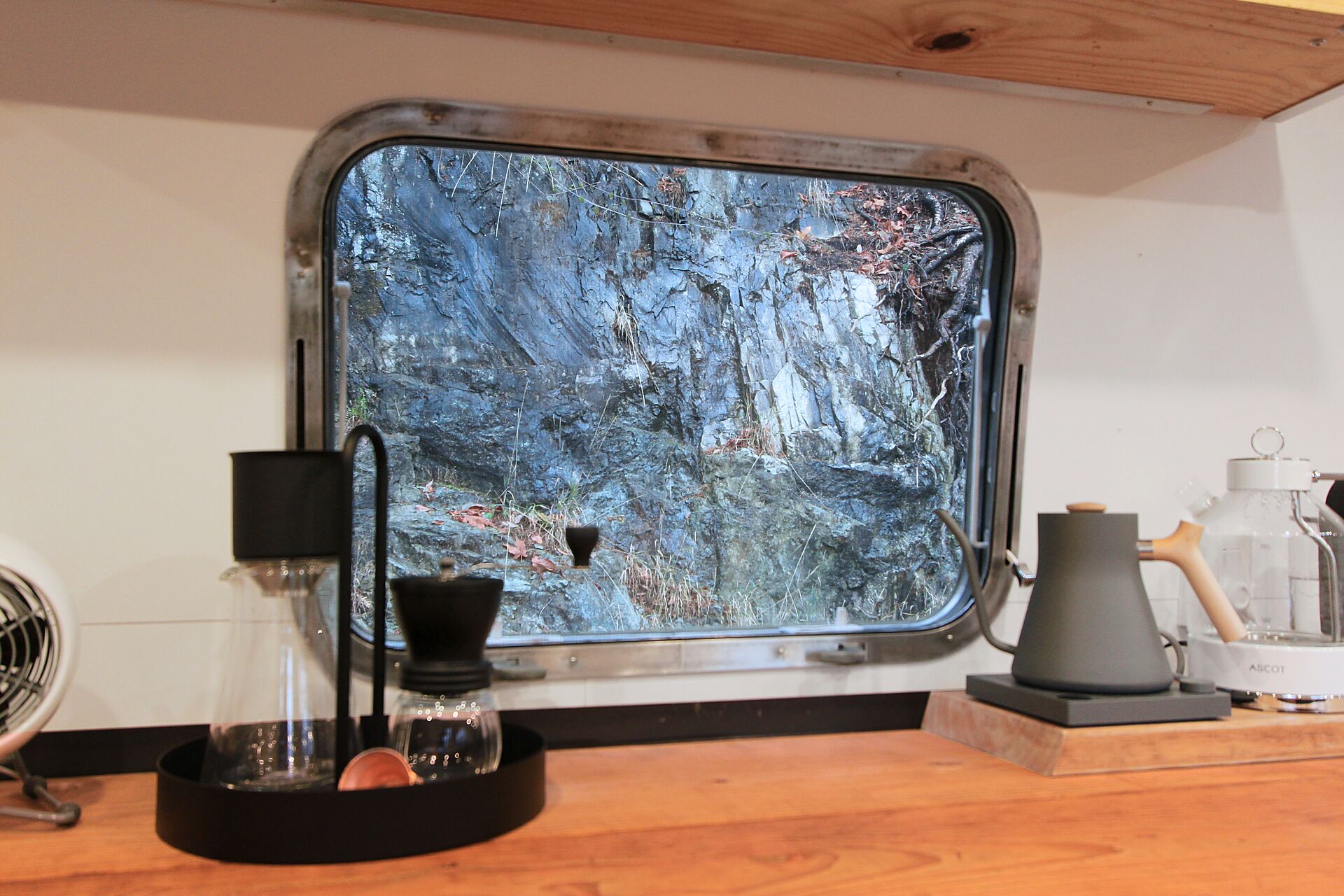 Una cocina con un ventanal grande, cafetera y ventilador.