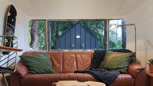 A cozy room with a brown leather sofa, a round woven rug, and a wooden table. - Wildernest Mountainside Airstream Getaway (Bowen Island)