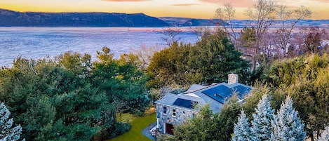 A house with a solar panel roof, surrounded by trees and a view of a body of water.