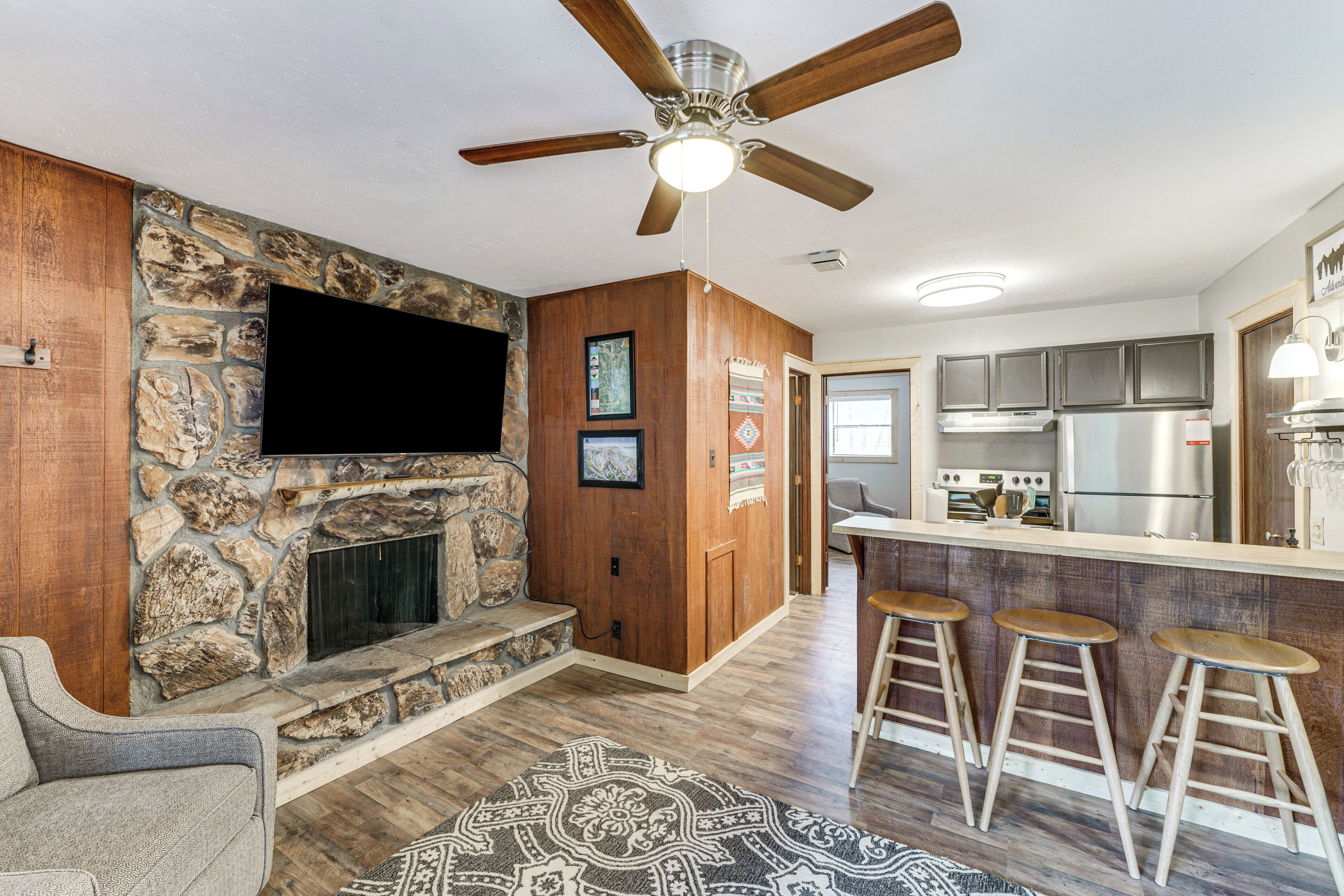 A modern kitchen with a stone wall, a built-in TV, and a bar area with stools.