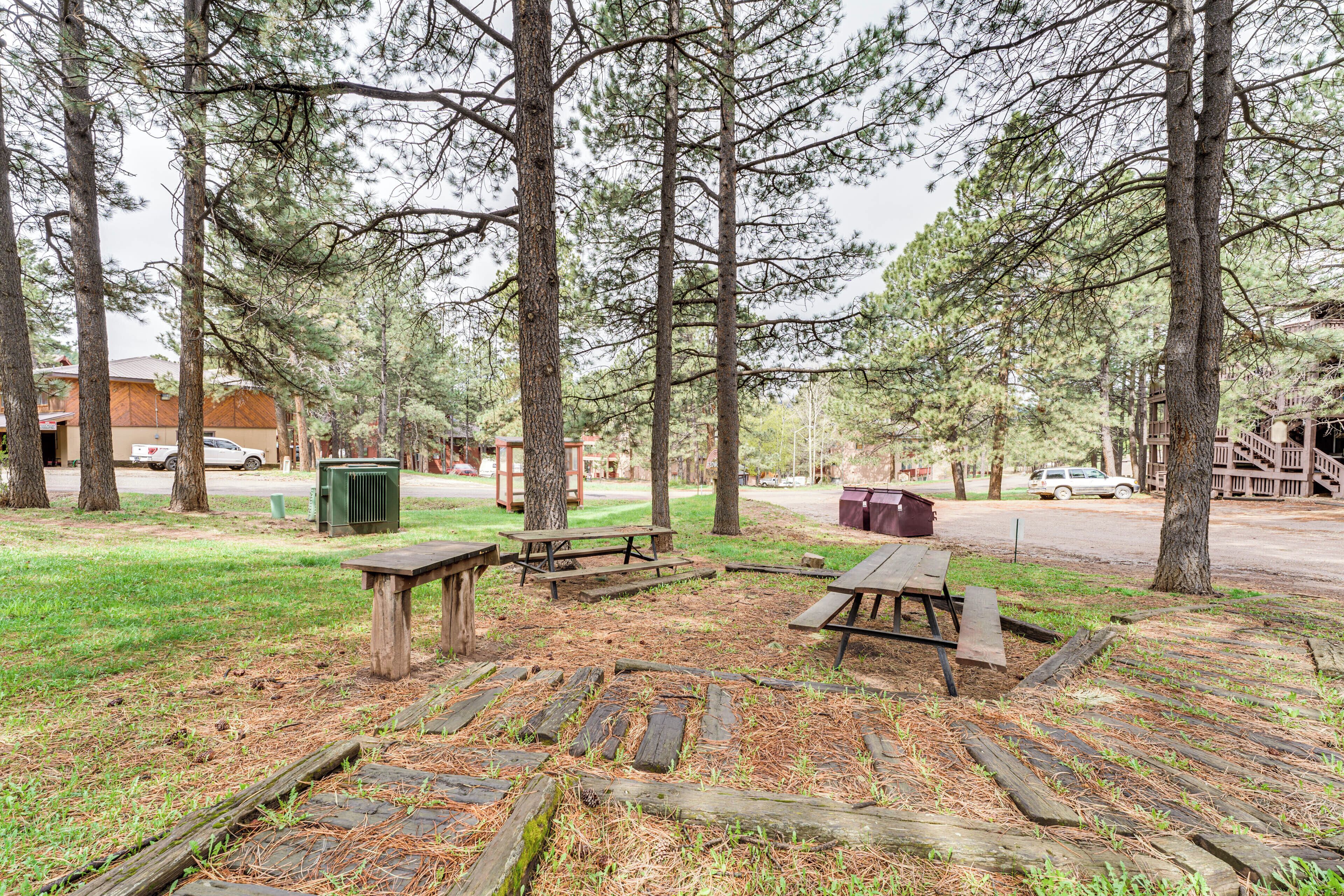 A park with picnic tables, a playground, and a building in the background.