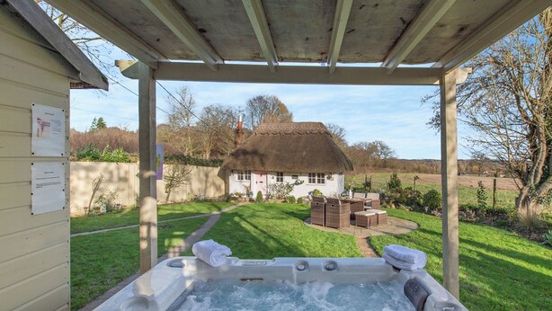 A hot tub with a view of a thatched-roof house and a grassy yard. - Brittons Hill Cottage (Kenardington, near Ashford)