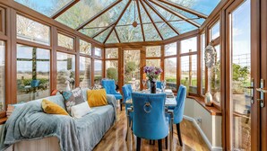 A conservatory with a wooden ceiling, a dining table set with chairs, and a sofa with cushions. - Brittons Hill Cottage (Kenardington, near Ashford)