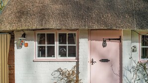 A quaint cottage with a thatched roof, a pink door, and a white brick wall. - Brittons Hill Cottage (Kenardington, near Ashford)