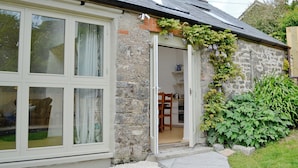 A stone house with a large window, a door leading to an interior, and a garden area with greenery. - 2 bedroom accommodation in Valast Hill, near Stackpole (Valast Hill, near Stackpole)