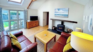 A spacious living room with a high ceiling, wooden beams, a fireplace, a television, and a large window overlooking a garden. - 2 bedroom accommodation in Valast Hill, near Stackpole (Valast Hill, near Stackpole)