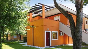 A modern two-story building with a red door, a covered outdoor area, and a staircase leading to the upper floor. - 2 bedroom gorgeous apartment in Bibione (Bibione)