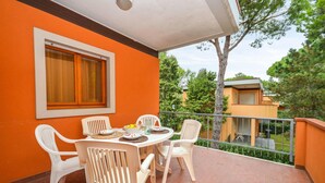A balcony with a table and chairs, a window, and a view of trees and buildings. - 2 bedroom gorgeous apartment in Bibione (Bibione)