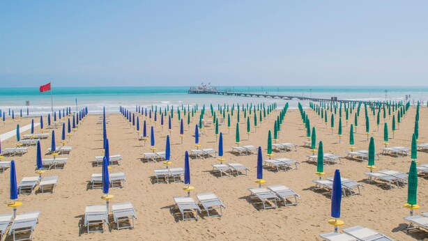A beach with rows of sun loungers and umbrellas, a pier in the distance, and a clear sky. - 2 bedroom gorgeous apartment in Bibione (Bibione)