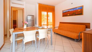 A compact living space with a dining area, a sofa, a painting, and a refrigerator. - 2 bedroom gorgeous apartment in Bibione (Bibione)