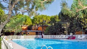 A swimming pool with a white fence, lounge chairs, and a building with orange walls in the background. - 2 bedroom gorgeous apartment in Bibione (Bibione)
