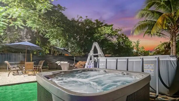 Een hottub met waterval, omringd door een omheind gebied met buitenmeubels en een palmboom.