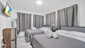 Hotelkamer met twee bedden, grijze beddengoed, een houten kast, een flatscreen televisie en grijze gordijnen.