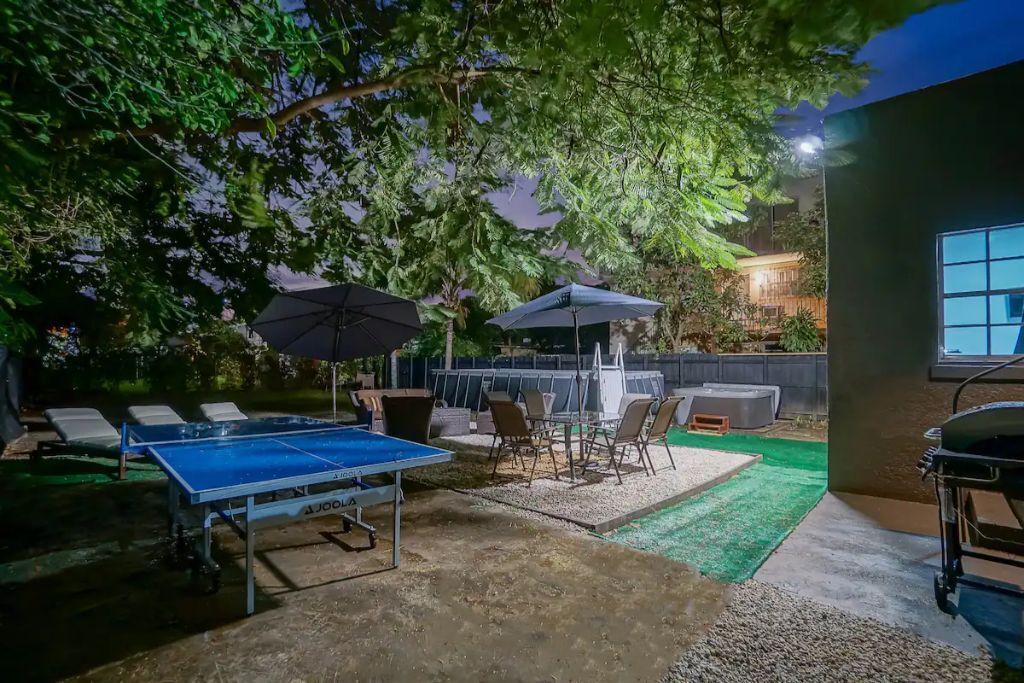 Un espace extérieur aménagé avec une table de ping-pong, des chaises, des parasols et une piscine.
