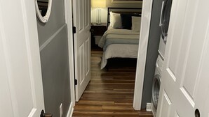 Ein schmaler Flur mit Holzboden führt zu einem Schlafzimmer mit Bett und Nachttisch.