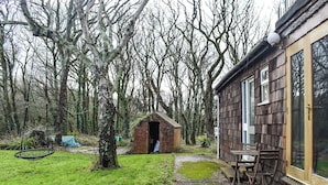 A rustic wooden building with a brick extension, a swing, and a gravel path leading to a wooden bench and table.